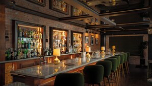 Een bar met een lange toonbank, meerdere flessenplanken en groene barkrukken.