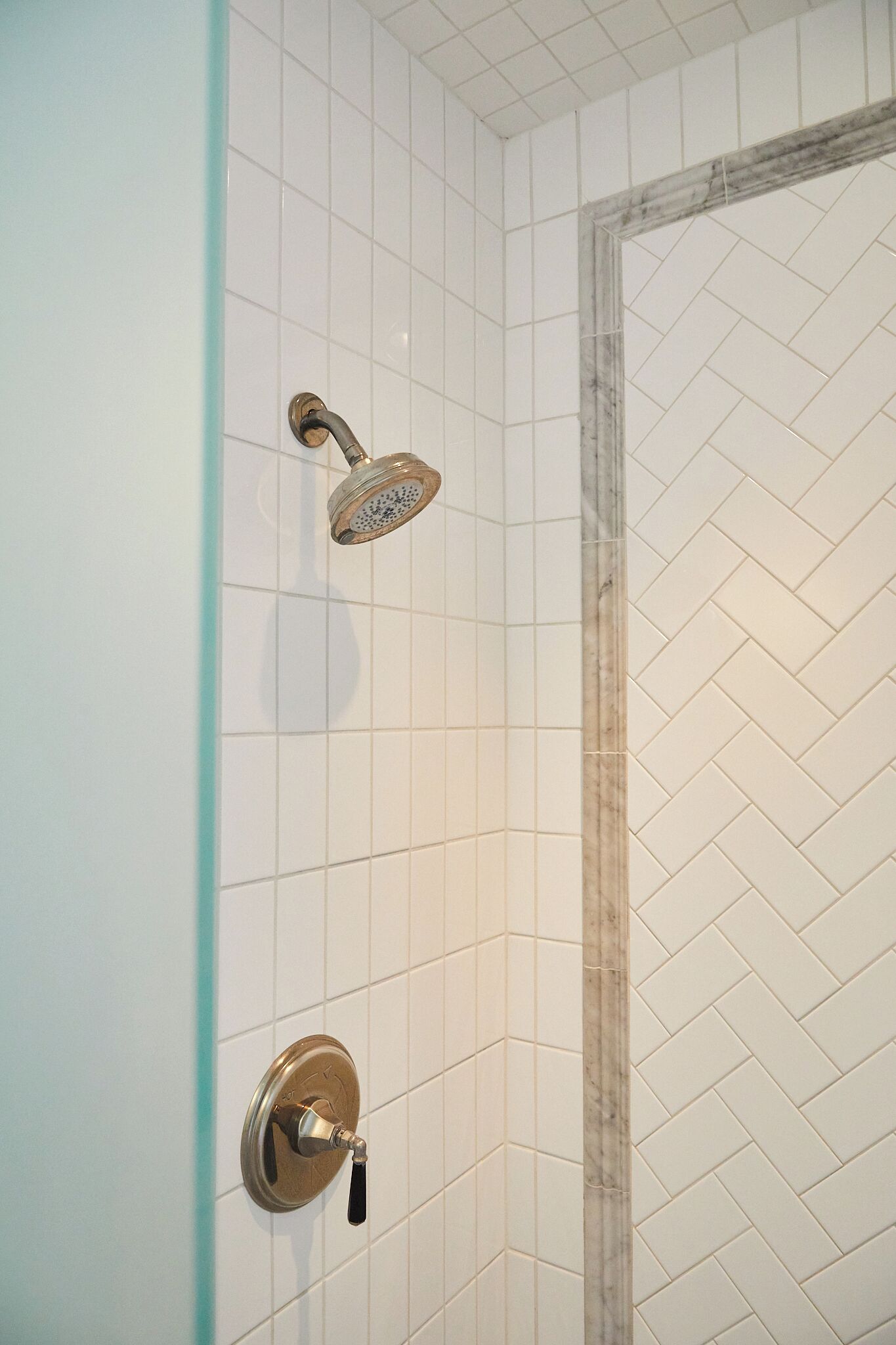 A bathroom with white herringbone tiles, a shower with a handheld showerhead, and a wall-mounted faucet.