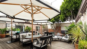 Een terras buiten met houten vloer, tafels, stoelen en parasols voor beschutting.