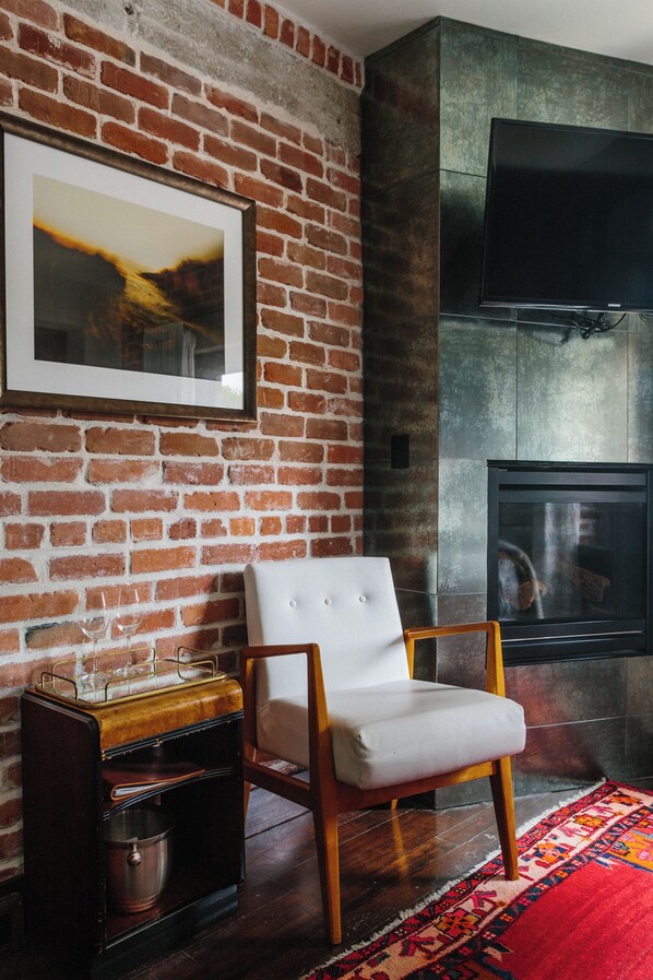 Una sala de estar con pared de ladrillo, chimenea, televisor, sillón blanco y radio antigua.