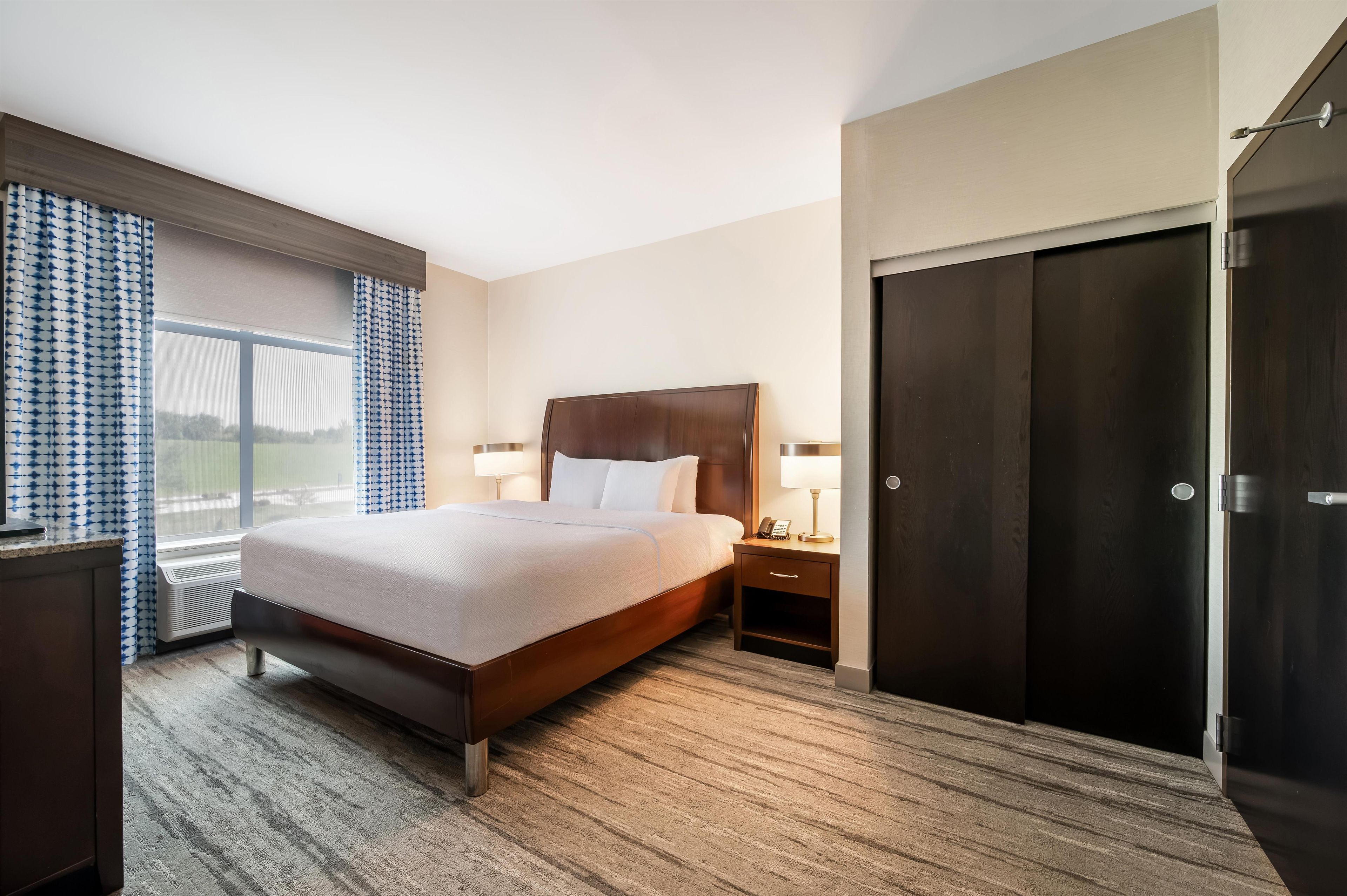 A hotel room with a large bed, bedside tables with lamps, a wardrobe, and a window with curtains.