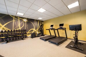 Een sportschool met loopbanden, een hometrainer en een muur vol gewichten.