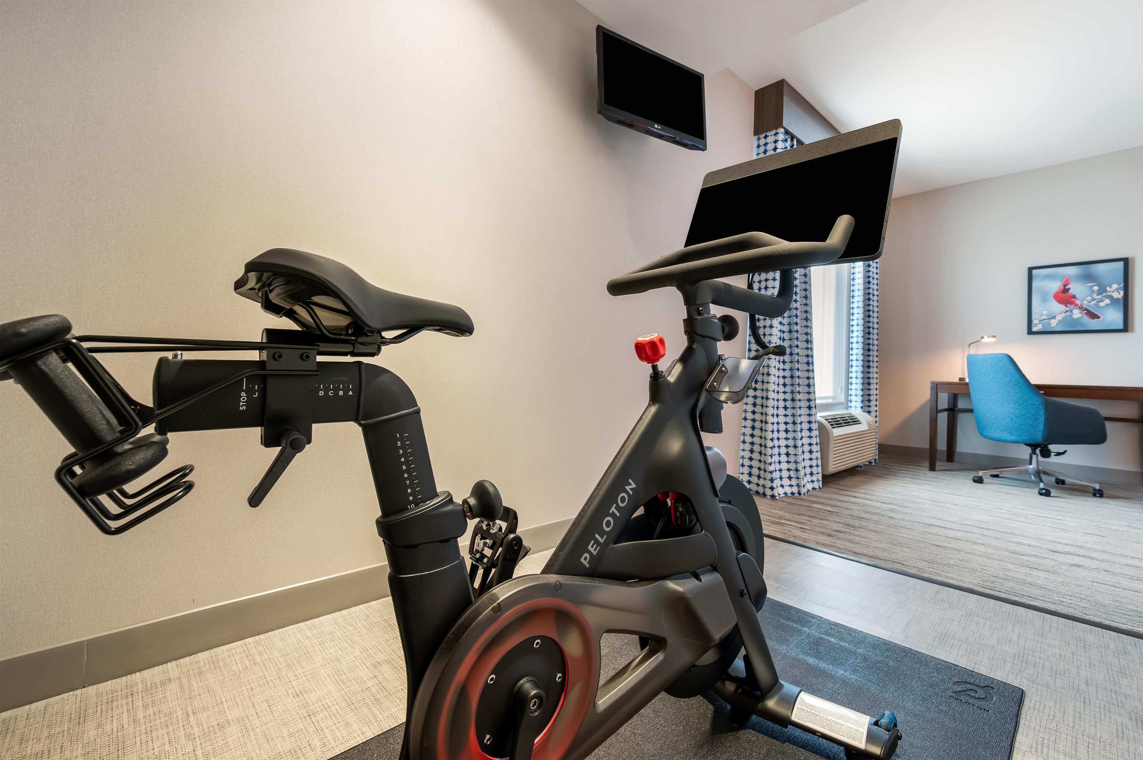 Una bicicleta estática en una habitación con una televisión, una silla y una ventana con cortinas.
