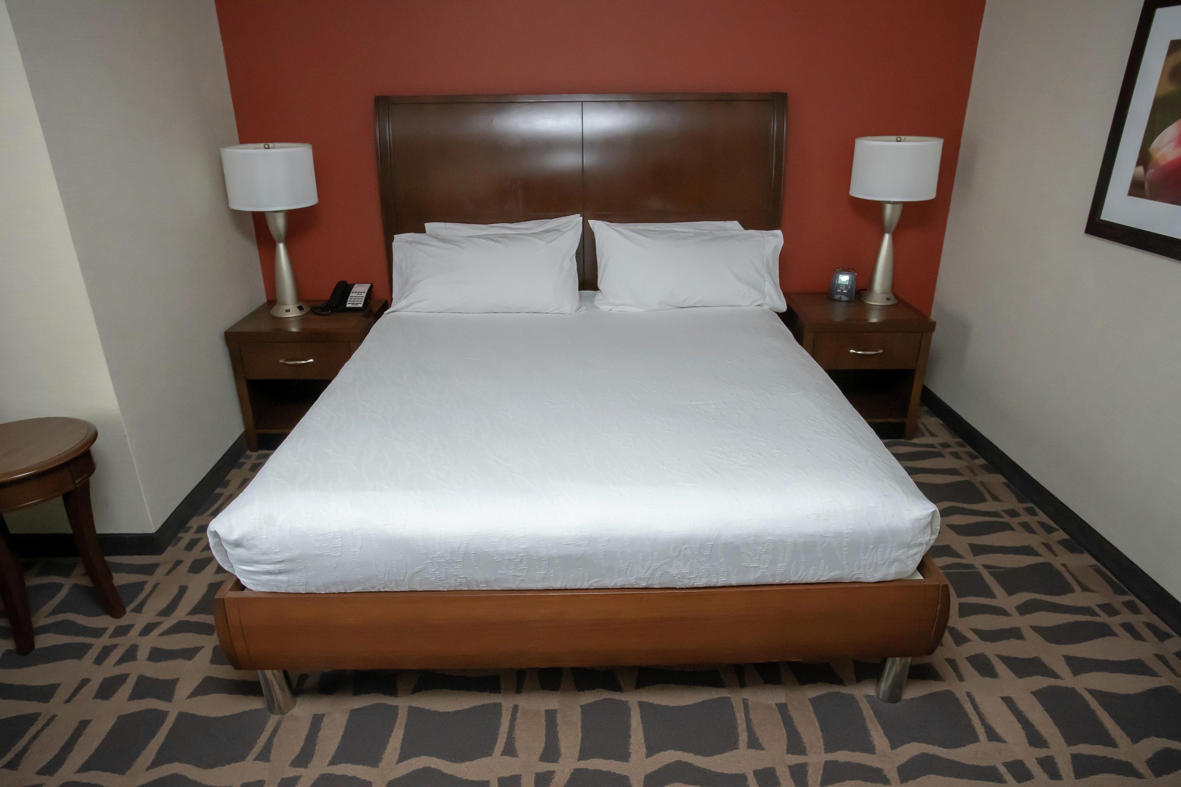 Habitación de hotel con una cama grande, dos mesitas de noche con lámparas, teléfono junto a la cama y un banco al pie de la cama.