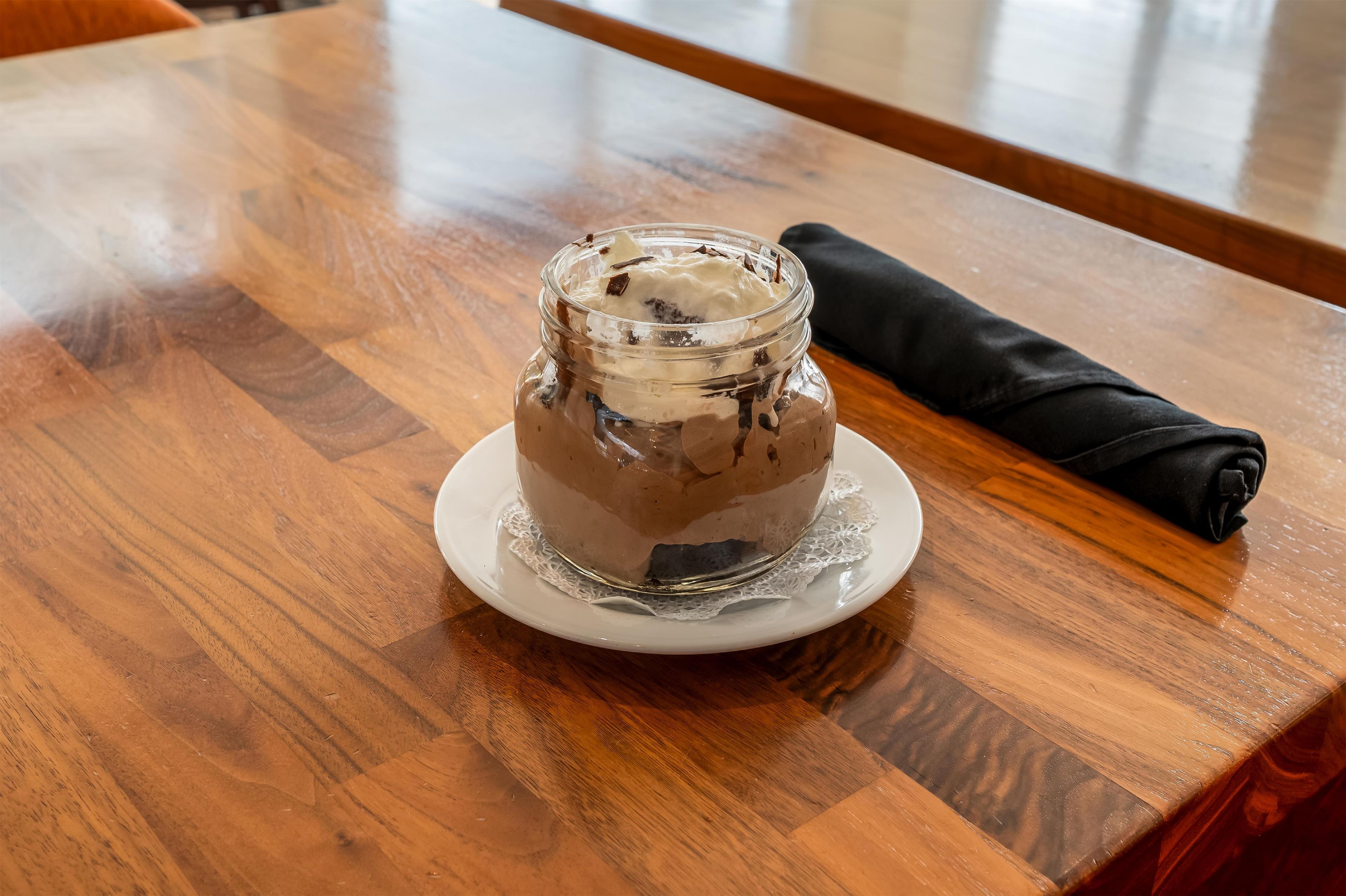 A dessert in a glass jar on a white plate, placed on a wooden table.