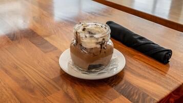 A dessert in a glass jar on a white plate, placed on a wooden table.
