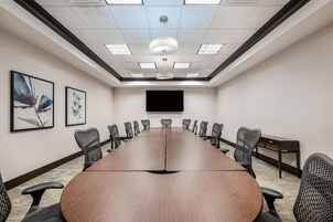 Un salón de conferencias con una larga mesa, sillas, una pantalla de televisión y obras de arte en las paredes.