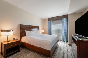 Ein Hotelzimmer mit einem Bett, Nachttischlampen, einem Schreibtisch mit Telefon, einem Fenster mit gemusterten Vorhängen und einem Fernseher.