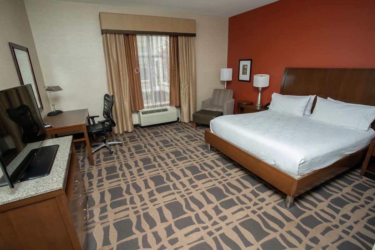 Een hotelkamer met een bed, bureau, stoel en een groot raam met gordijnen.