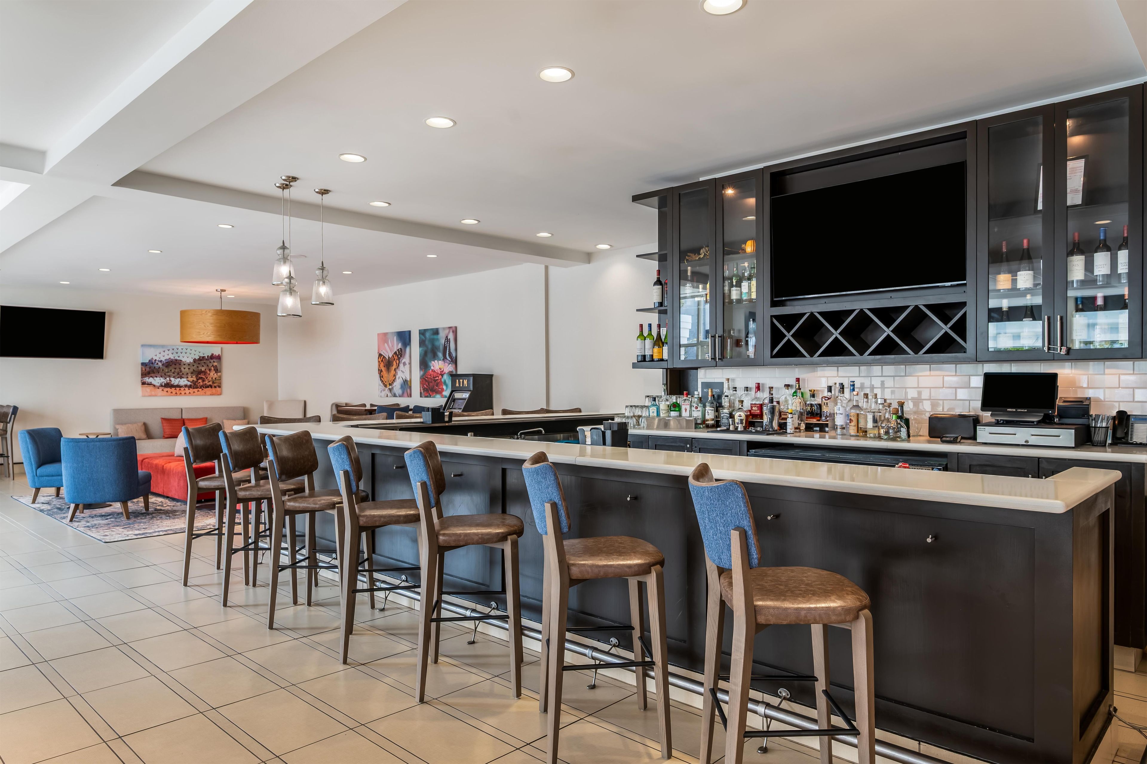 A modern kitchen with a bar area, equipped with bar stools and a countertop stocked with bottles.