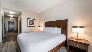 A hotel room with a large bed, two bedside lamps, a wooden headboard, a framed picture on the wall, and a door leading to another room.