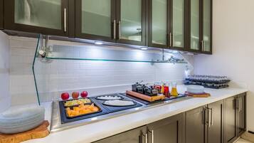 Una cocina moderna con un armario de vidrio, un salpicadero de azulejos blancos y una barra de desayuno con diversos alimentos y condimentos.