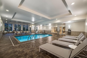 Un área interior de piscina moderna con sillones de descanso, una piscina y una fuente de agua.