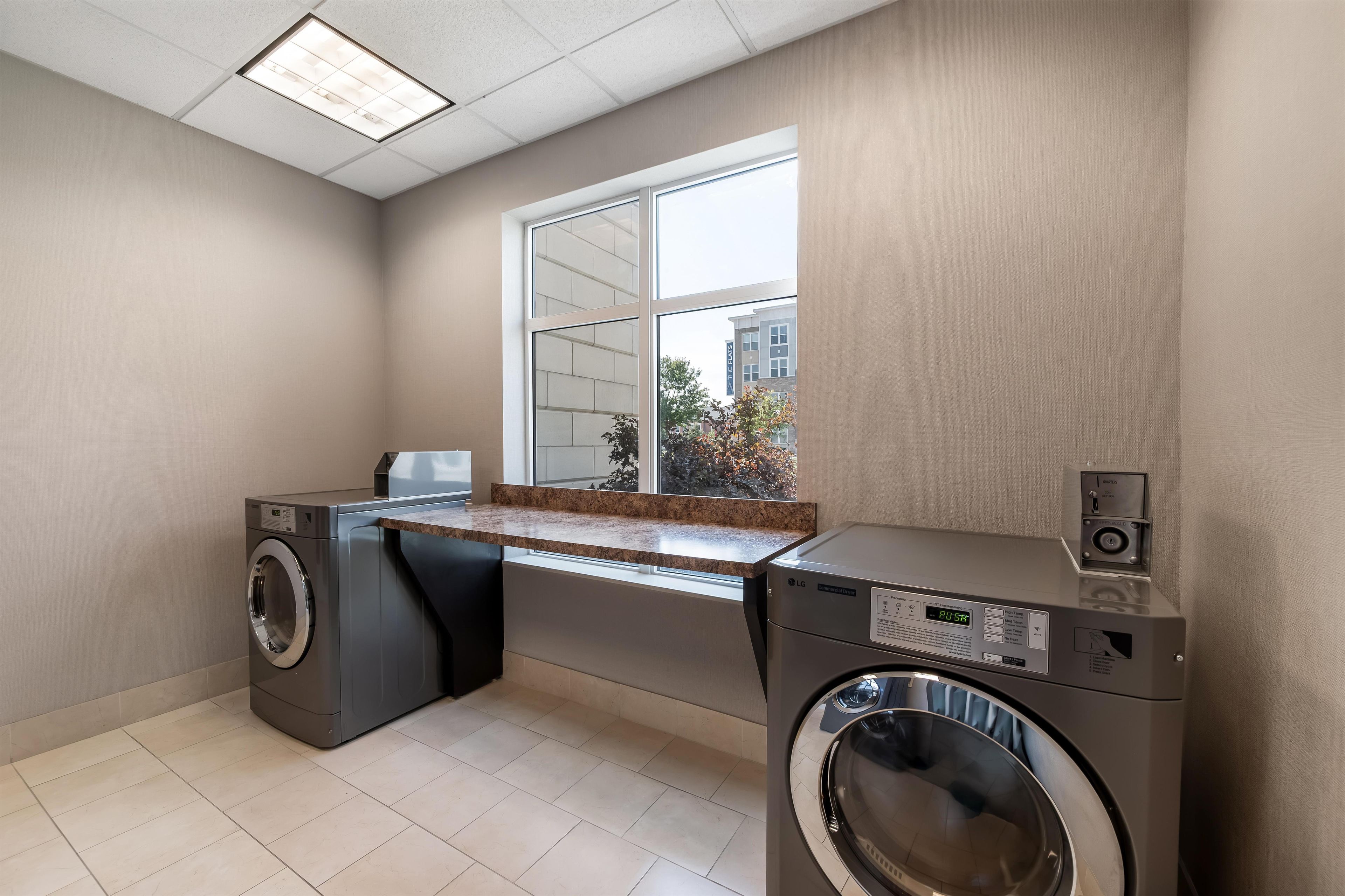 A laundry room with two washing machines, a countertop, and a window with a view of buildings.