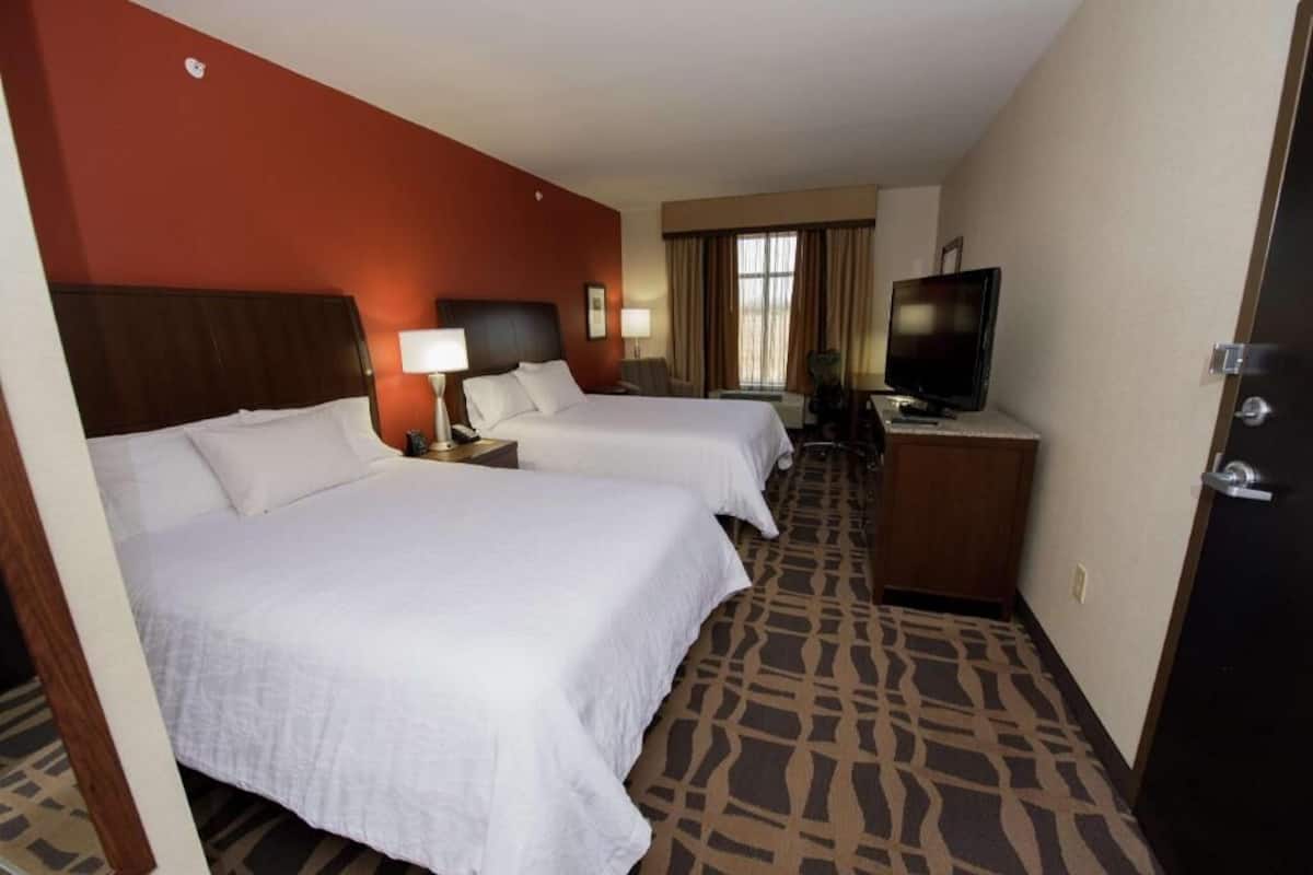 Een hotelkamer met twee bedden, een televisie, een bureau en een kamerbreed tapijt met een patroon.