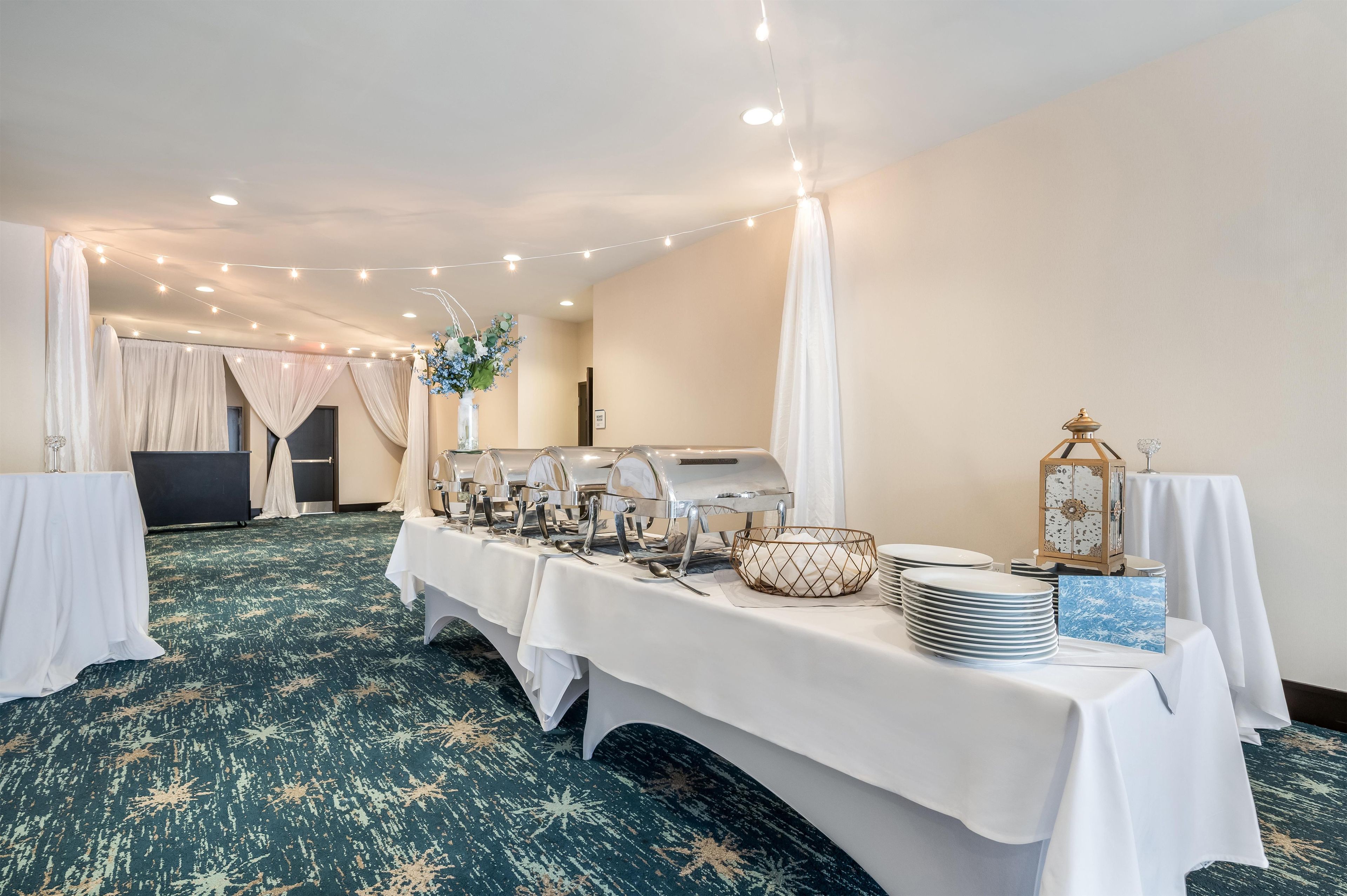 A banquet hall with a long table set for a buffet, featuring a buffet station, a decorative vase, and a lantern.