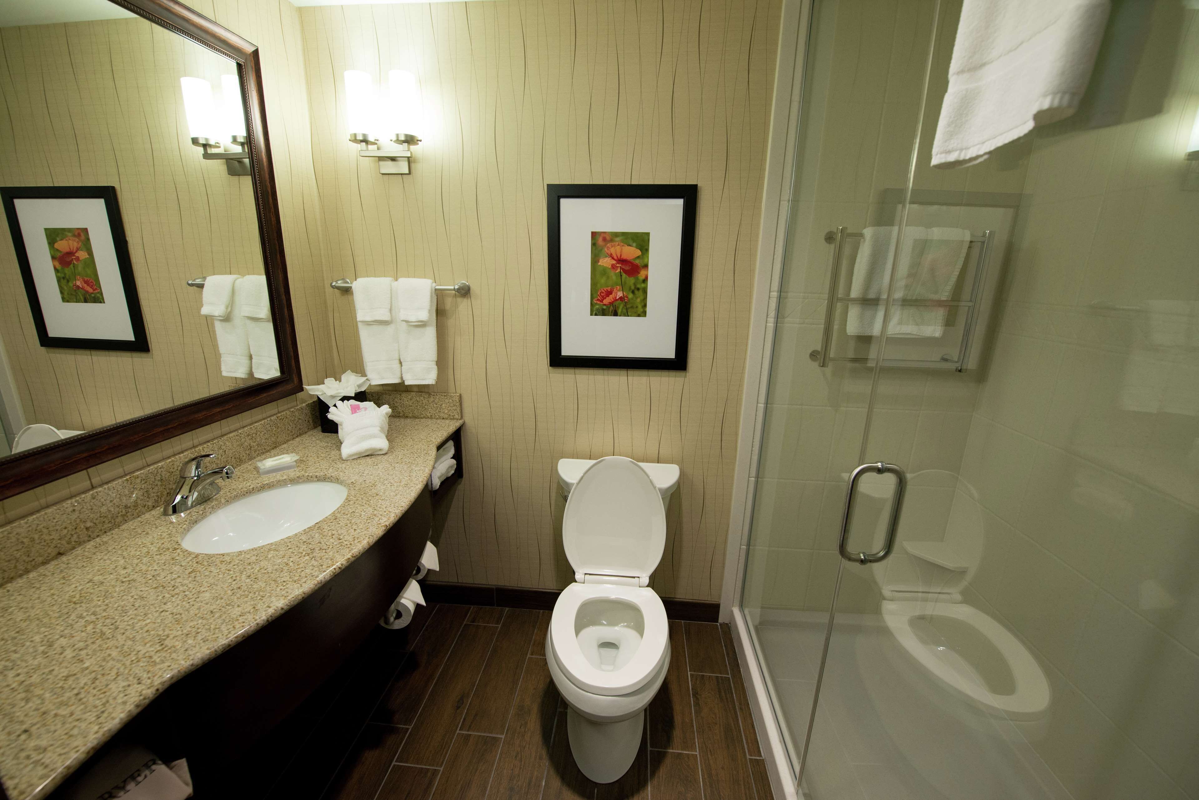 A bathroom with a sink, toilet, and shower. There are framed pictures on the wall and a towel rack.