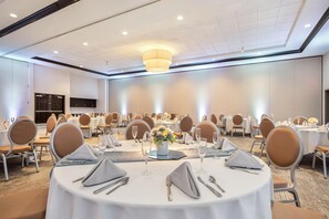 Ein Festsaal mit runden Tischen, gedeckt für ein Essen, ausgestattet mit Stühlen, Tischdeckware und einem zentralen Kronleuchter.