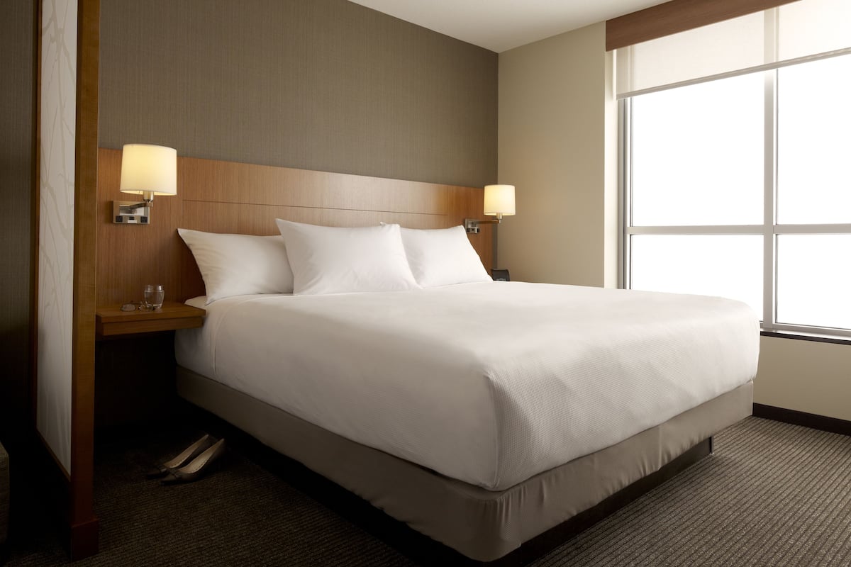 A hotel room with a large bed, two bedside lamps, a nightstand, and a window with daylight.