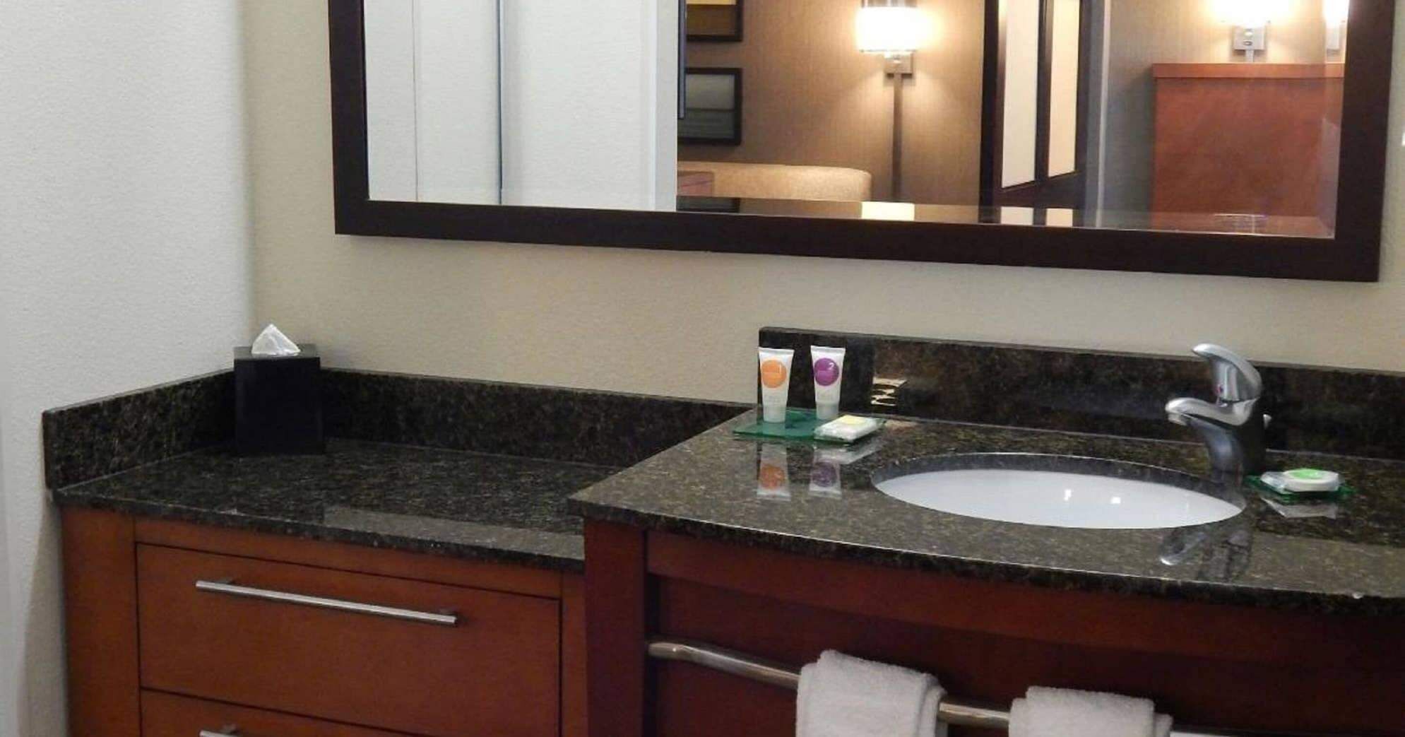 A bathroom with a granite countertop, a sink, a mirror, and a towel rack.