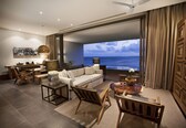 A modern living room with a large window overlooking the sea, a sofa, a coffee table, and a dining area.