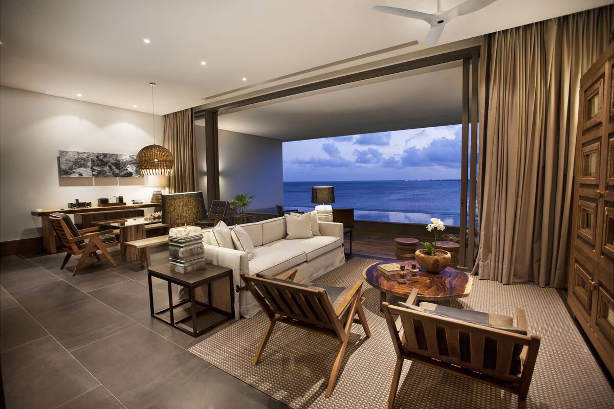 A modern living room with a large window overlooking the sea, a sofa, a coffee table, and a dining area.