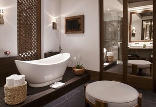 A modern bathroom with a freestanding bathtub, a round wooden stool, and a large mirror.