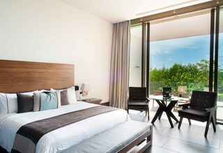 A modern hotel room with a large bed, a desk, and a balcony with a view of greenery.