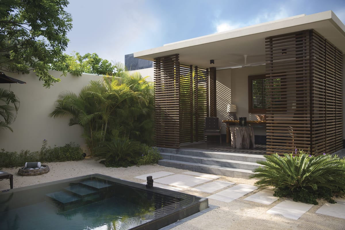 A modern outdoor pool area with a built-in seating area, surrounded by lush greenery and a minimalist architectural design.