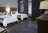 A hotel room with two beds, a bedside table with a lamp, a small table with a candle, and a wall-mounted artwork.