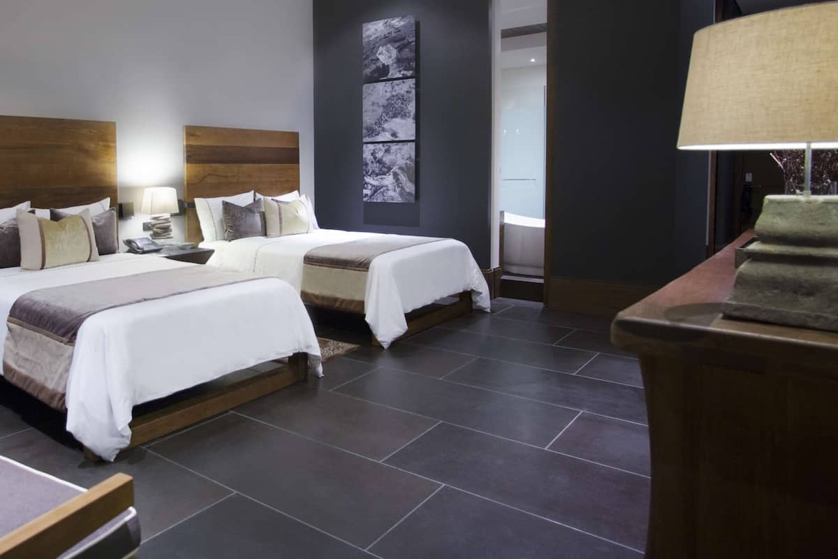 A hotel room with two beds, a bedside table with a lamp, a small table with a candle, and a wall-mounted artwork.
