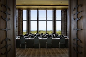 A conference room with a large table, chairs, and a view of the outdoors through large windows.