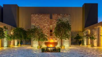 A courtyard with a central fire feature, surrounded by trees and stone walls.