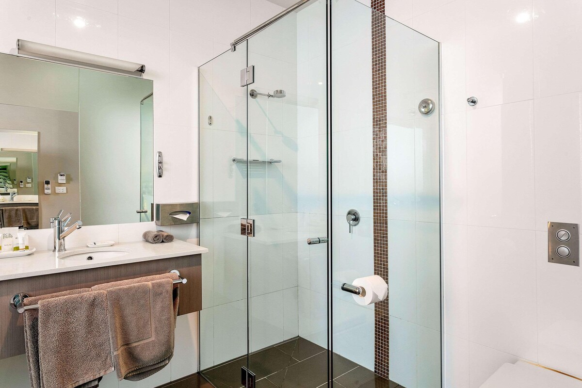 A modern bathroom with a glass-enclosed shower, a white sink, and a large mirror.