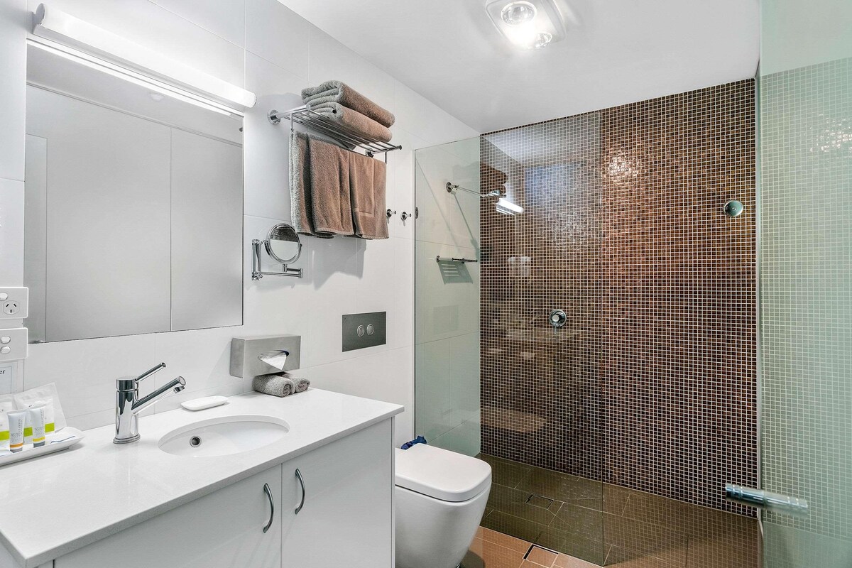 A modern bathroom with a white vanity, a glass shower enclosure, and a visible toilet.