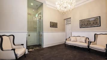 A hallway with two beige sofas, a chandelier, and framed artwork on the walls.