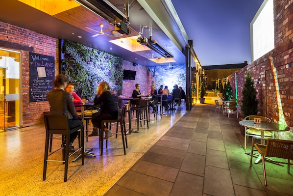 An outdoor seating area with brick walls and greenery, tables numbered 37 and 38, and a chalkboard sign.