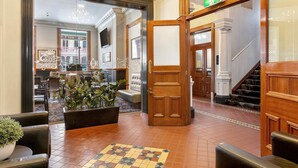 A lobby with a checkered floor, wooden doors, and a seating area with potted plants.