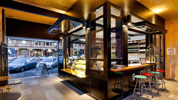 A modern cafe with a glass front display case, outdoor seating, and a visible street view.