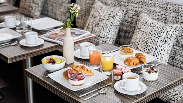 Une table en bois dressée pour le petit-déjeuner, avec des croissants, des fruits, du yaourt et du jus.