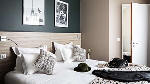 Une chambre d’hôtel avec un lit, des oreillers, un chapeau, un sac à main et deux tableaux encadrés accrochés au mur.