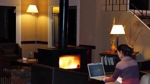 Ein gemütliches Wohnzimmer mit Kamin, einer Couch, einem Tisch und einer Person, die einen Laptop benutzt.
