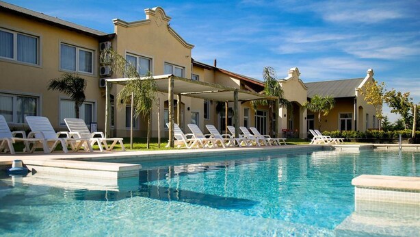 Ein Swimmingpool mit Liegestühlen und einer überdachten Sitzgelegenheit, umgeben von Gebäuden im mediterranen Baustil.