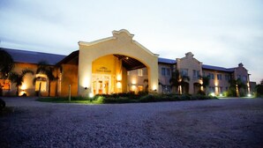 Ein Hotel mit Eingangsbereich, einer überdachten Laube, Palmen und einem Schotterweg.