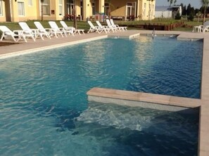 En swimmingpool med hvide liggestole og en fliseterrasse.