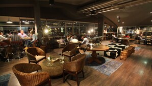 A spacious indoor seating area with wicker chairs and round tables, large windows offering city views, and a modern industrial ceiling design. - Casa Grande Hotel (La Paz)