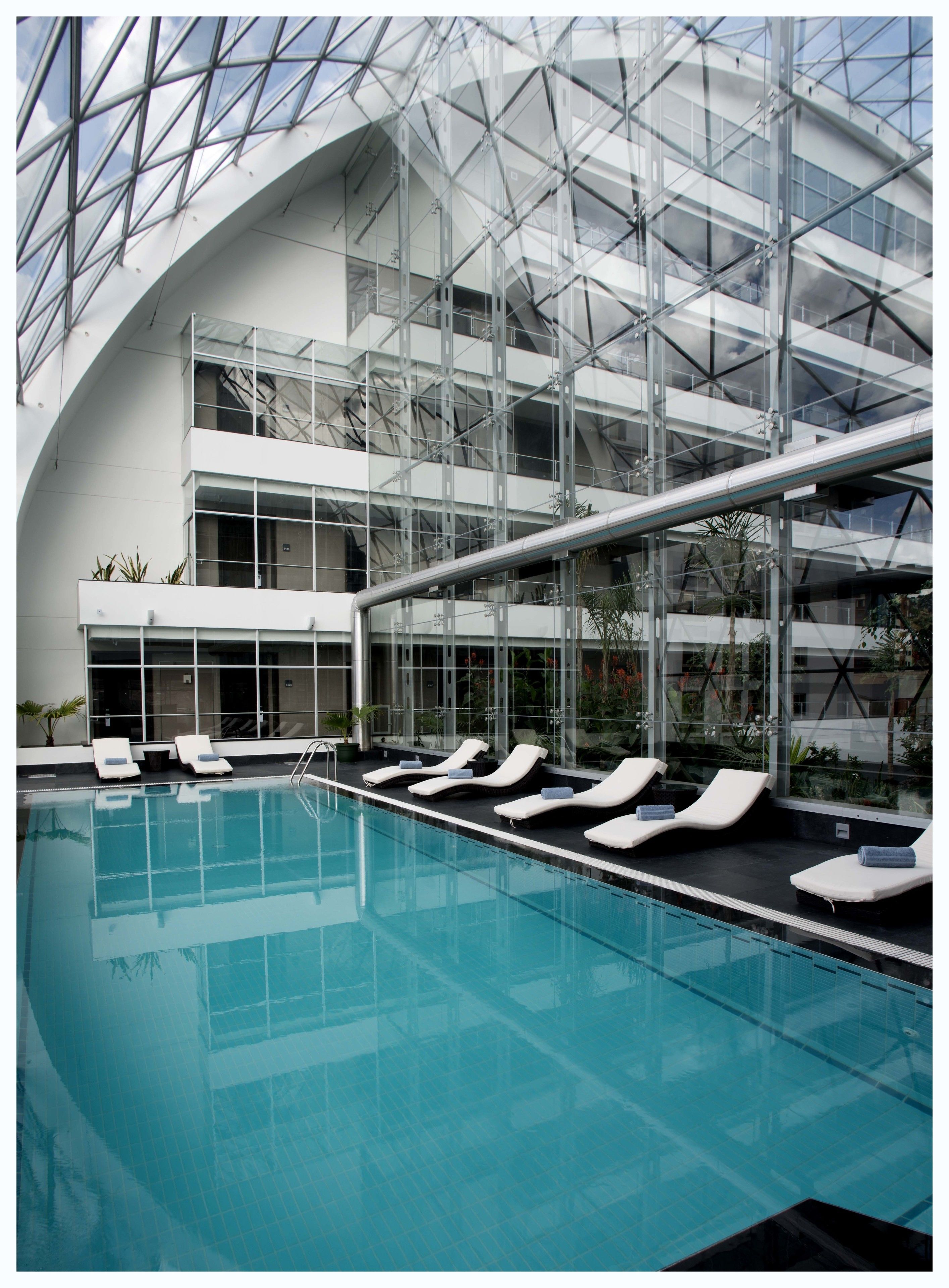 A modern indoor swimming pool with multiple levels of balconies and lounge chairs.