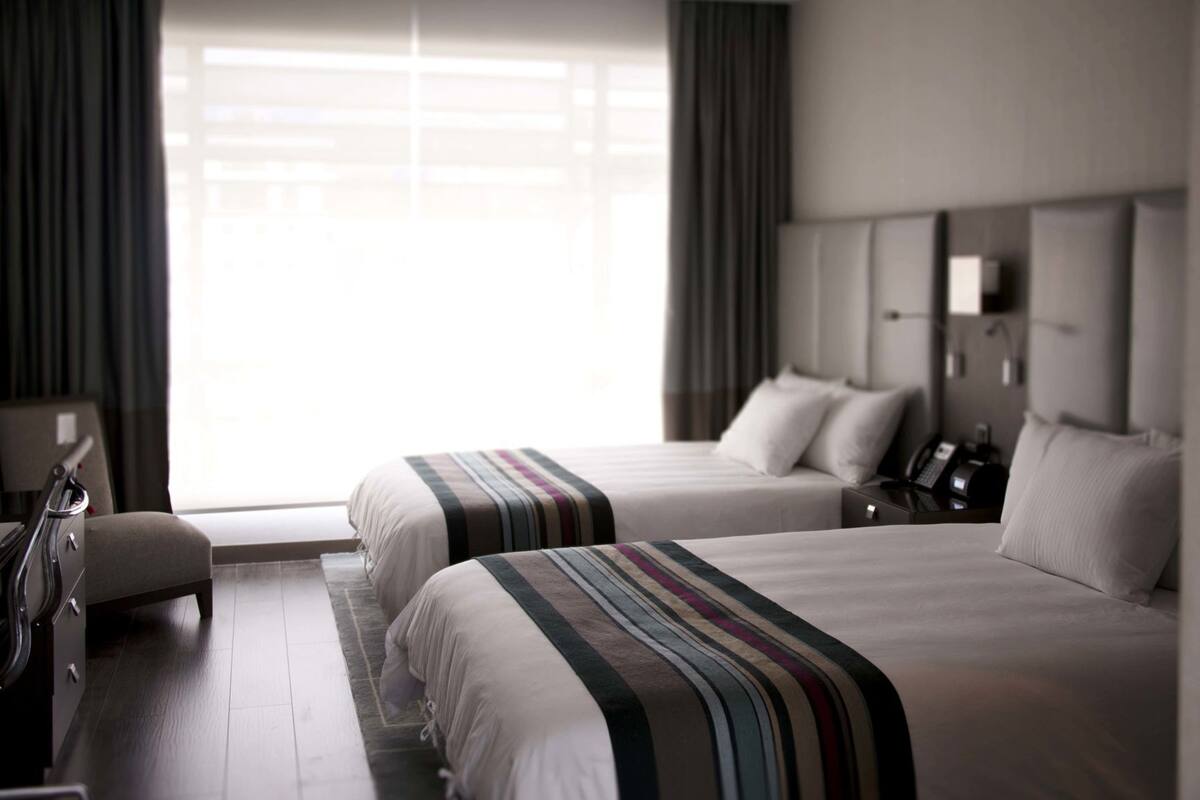 A hotel room with two beds, a desk, a chair, a telephone, and a window with curtains.