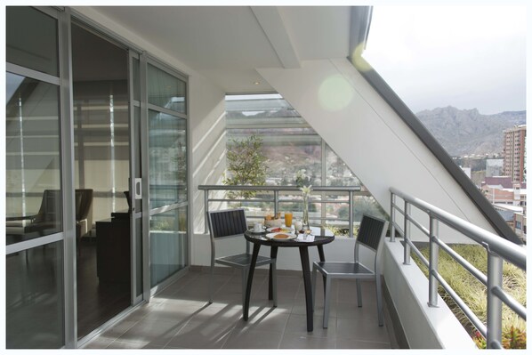 Un balcón con una mesa lista para el desayuno, una silla y vistas a la ciudad y las montañas.