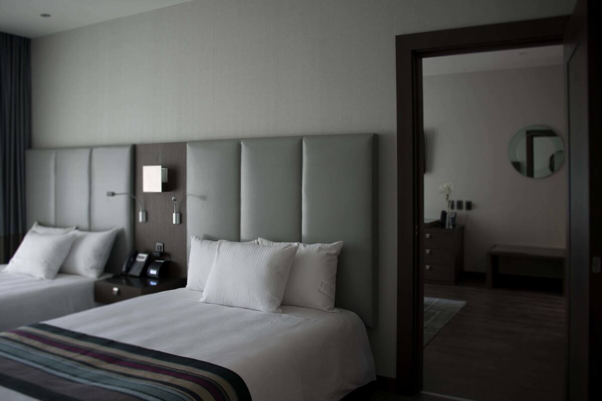 A hotel room with two beds, a large mirror, a bedside table with a phone, and a small desk with a lamp.